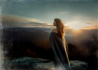 A mysterious witch stands atop the Smoky Mountains at sunset in late fall, her dark wool cloak billowing in the wind as she gazes into the distance, framed by golden light and autumnal hues.