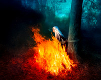 A white-haired woman bound to a tree by rope, surrounded by a large bonfire, is nonchalantly smoking a cigarette.