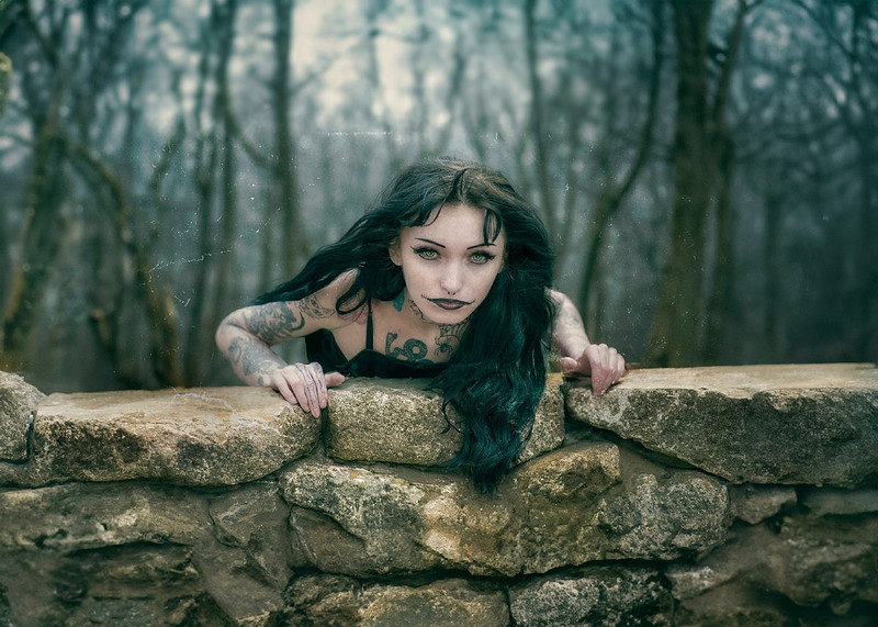 Occult-themed photo of a pale and frightening witch climbing a mossy stone wall in the mysterious Aokigahara forest.