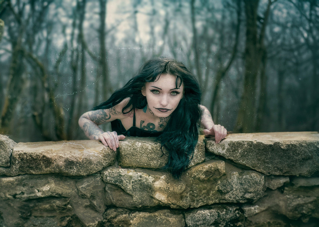 Occult-themed photo of a pale and frightening witch climbing a mossy stone wall in the mysterious Aokigahara forest.